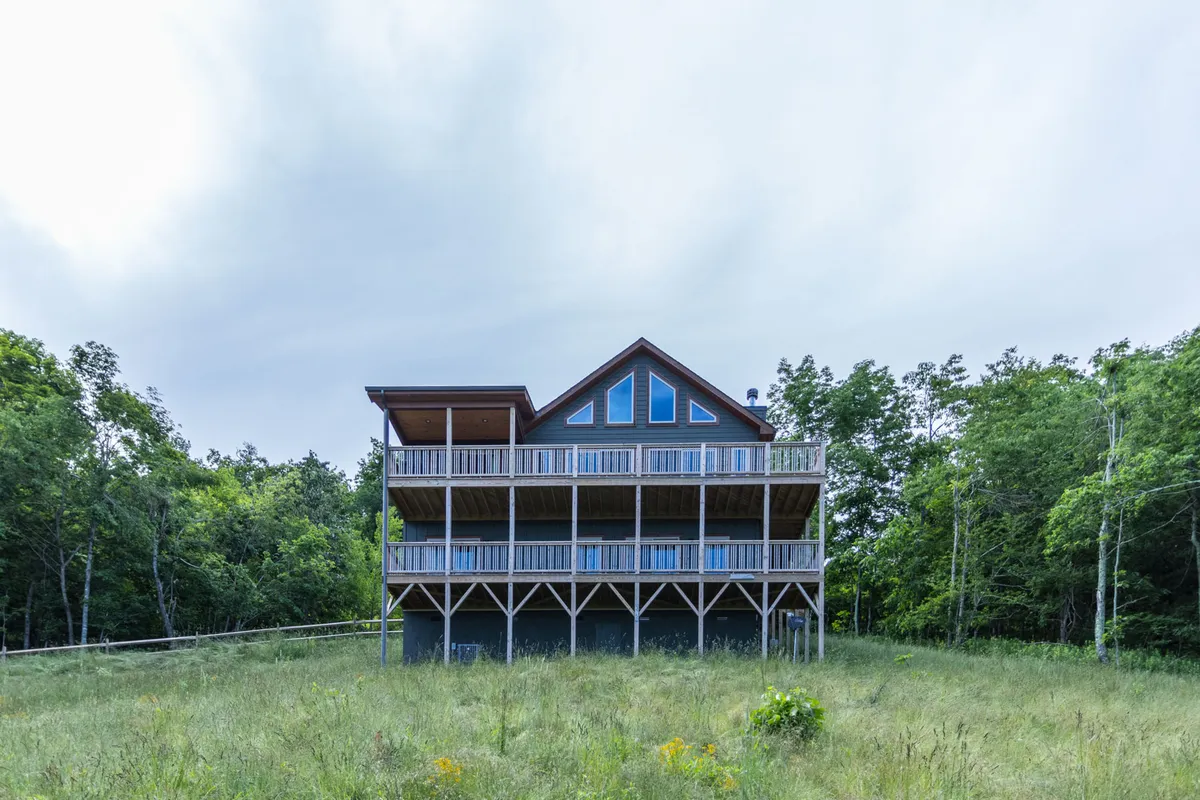 The image showcases the striking architectural design of the single-family house perched high on Appalachian Ski Mountain, with an expansive deck that overlooks lush greenery. The serene setting hints at activities like family gatherings, quiet mornings with coffee, and evenings spent stargazing or enjoying unforgettable sunsets from the balcony.