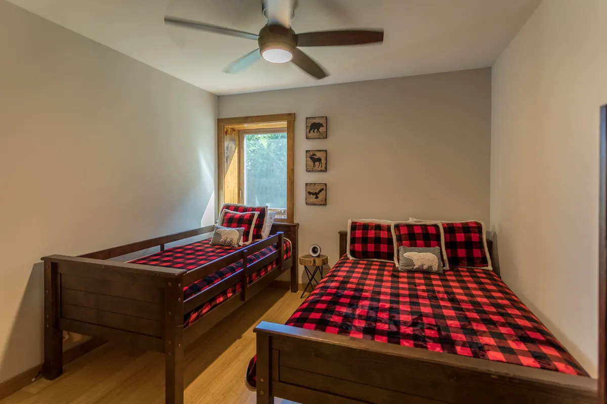 A cozy bunk-style room designed for children or friends, featuring built-in bunk beds with plaid bedding, a bright window letting in natural light, and playful animal-themed wall art. The space feels inviting and playful, perfect for sleepovers or sibling stays.