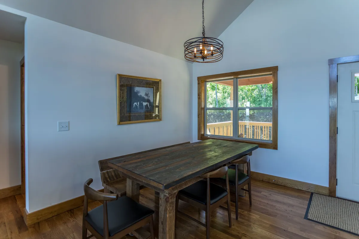 A wooden dining table sits beside a window that frames scenic views, complemented by elegant pendant lighting and displaying artwork that adds a touch of sophistication. The setting is warm and intimate, ideal for both celebratory meals and quiet moments.