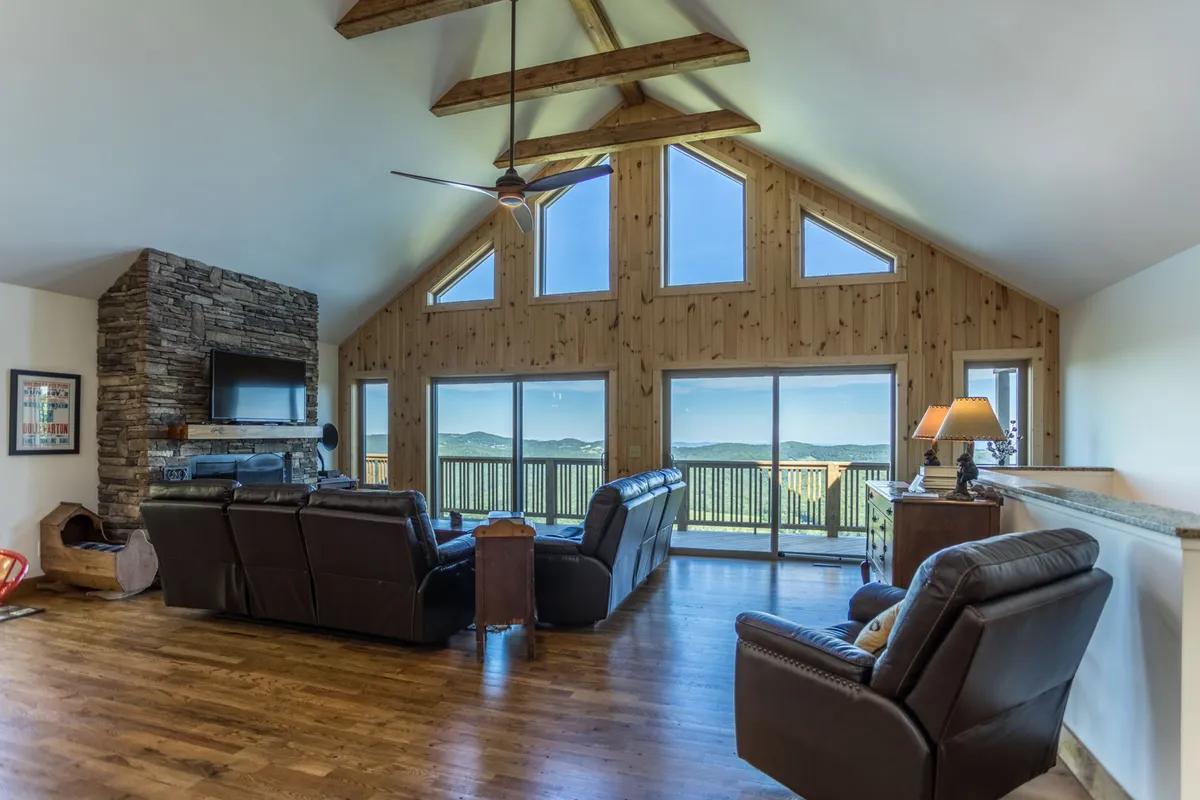 A comfortable seating area arranged around a stone fireplace, with large windows framing mountain views. The space feels serene and is ideal for unwinding with loved ones, watching sunsets, or enjoying fireside chats after a day out.